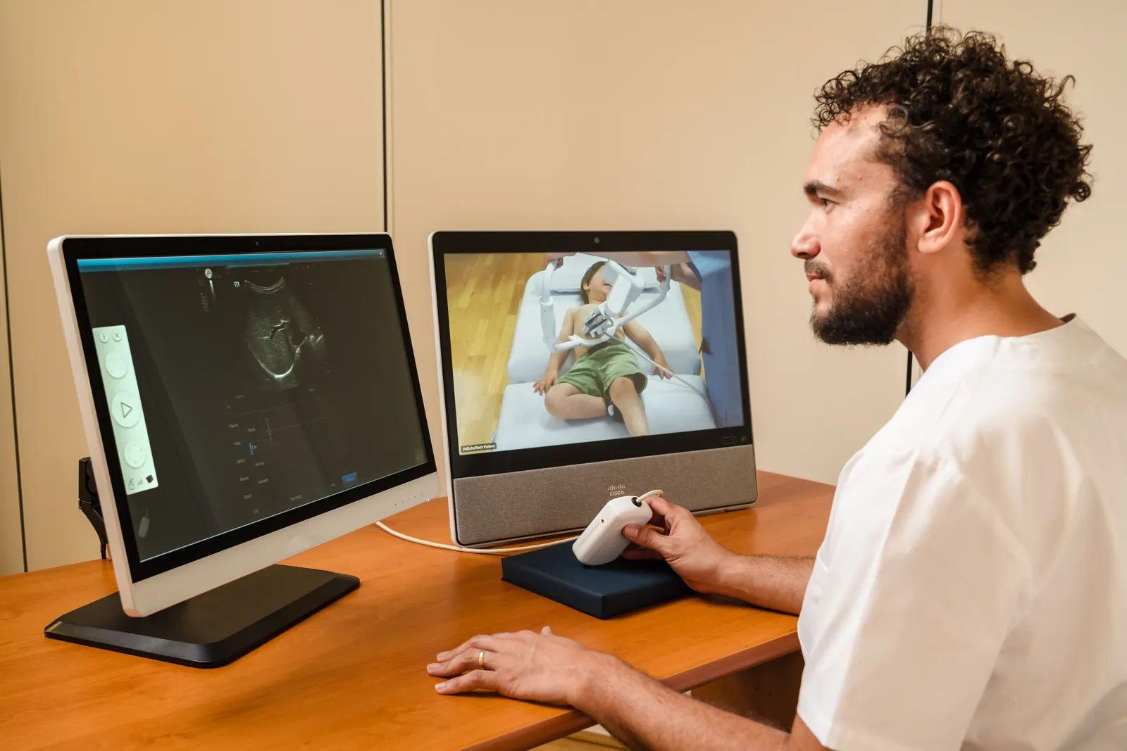 A specialist at the expert station follows a child's examination on screen, hand on the twin probe