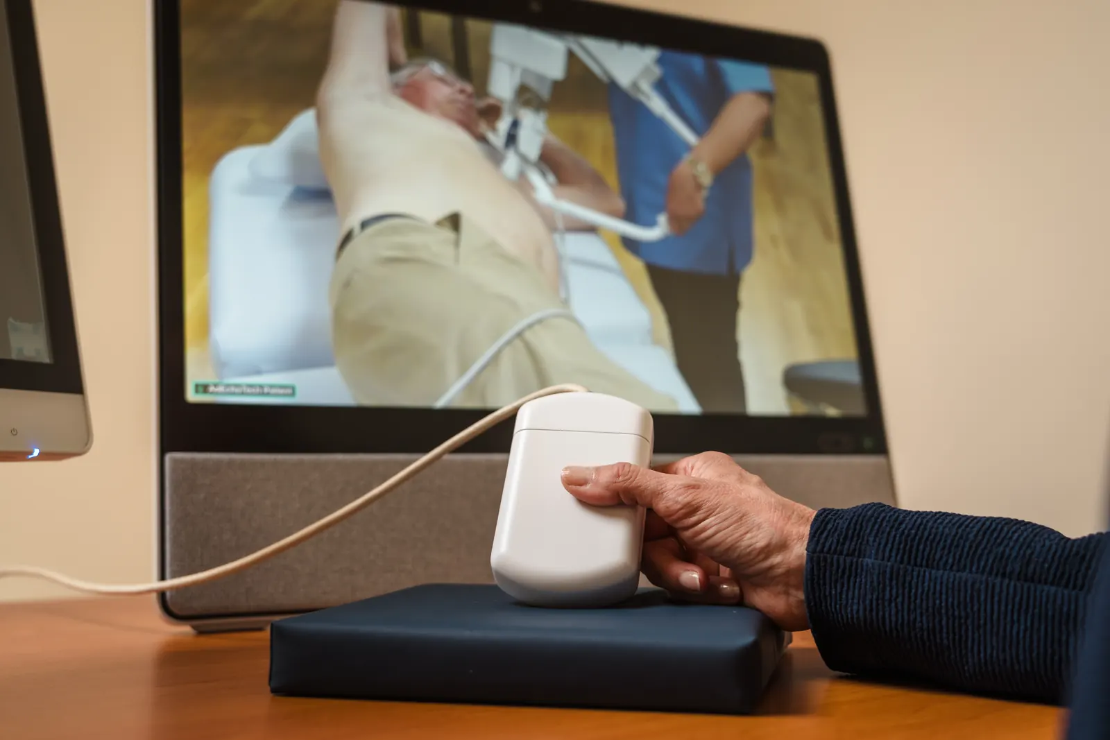 The twin probe in the specialist's hand, in front of the screen showing the patient's room