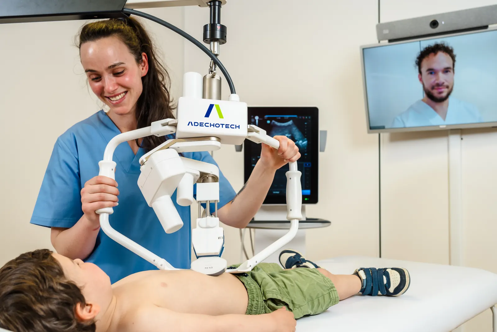 Paediatric examination with MELODY: a nurse positions the robotic arm on the abdomen of a child lying down, the specialist is on the videoconference screen
