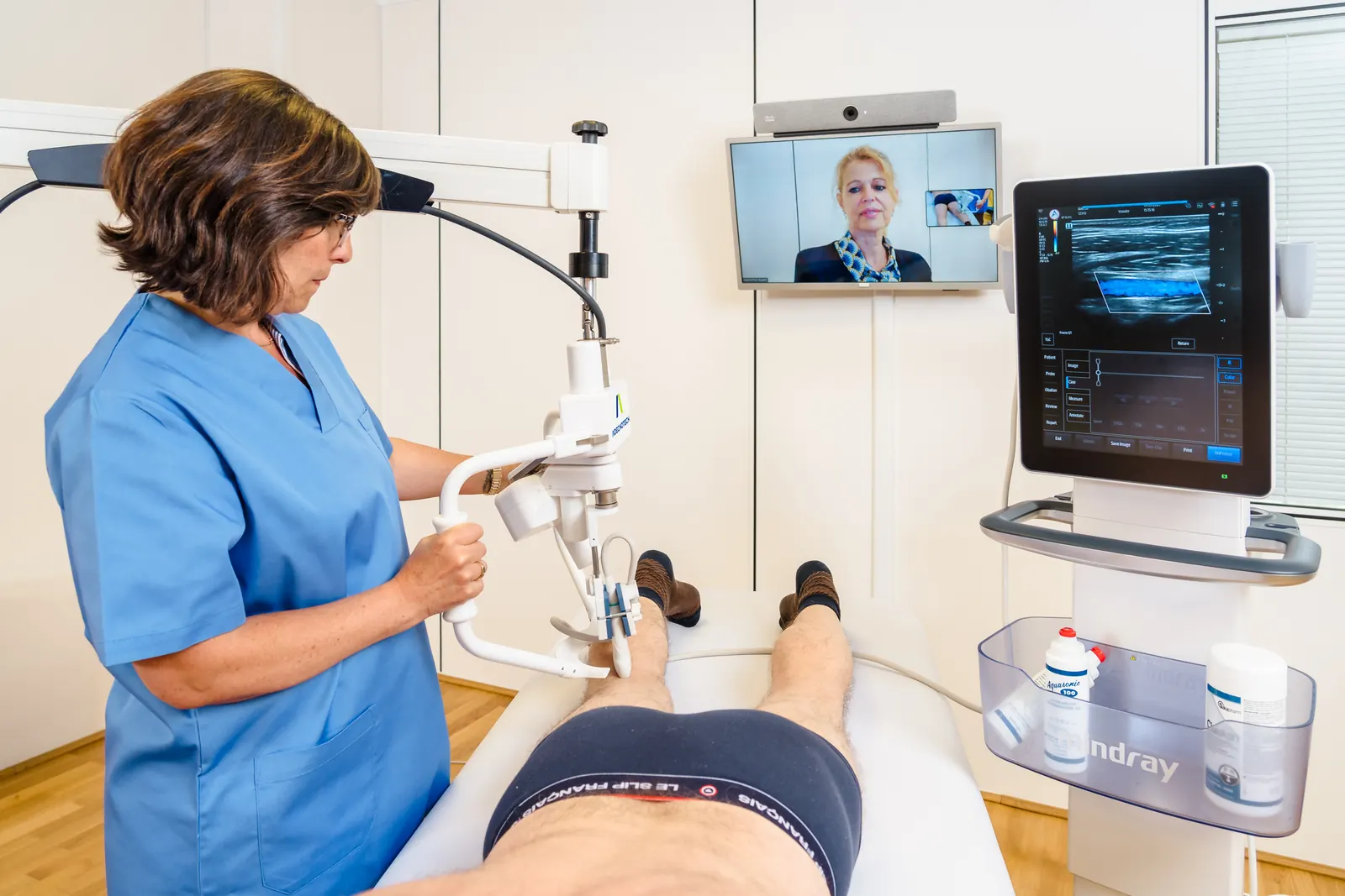 Vascular examination with MELODY: a nurse positions the robotic arm on a patient's leg next to the ultrasound system